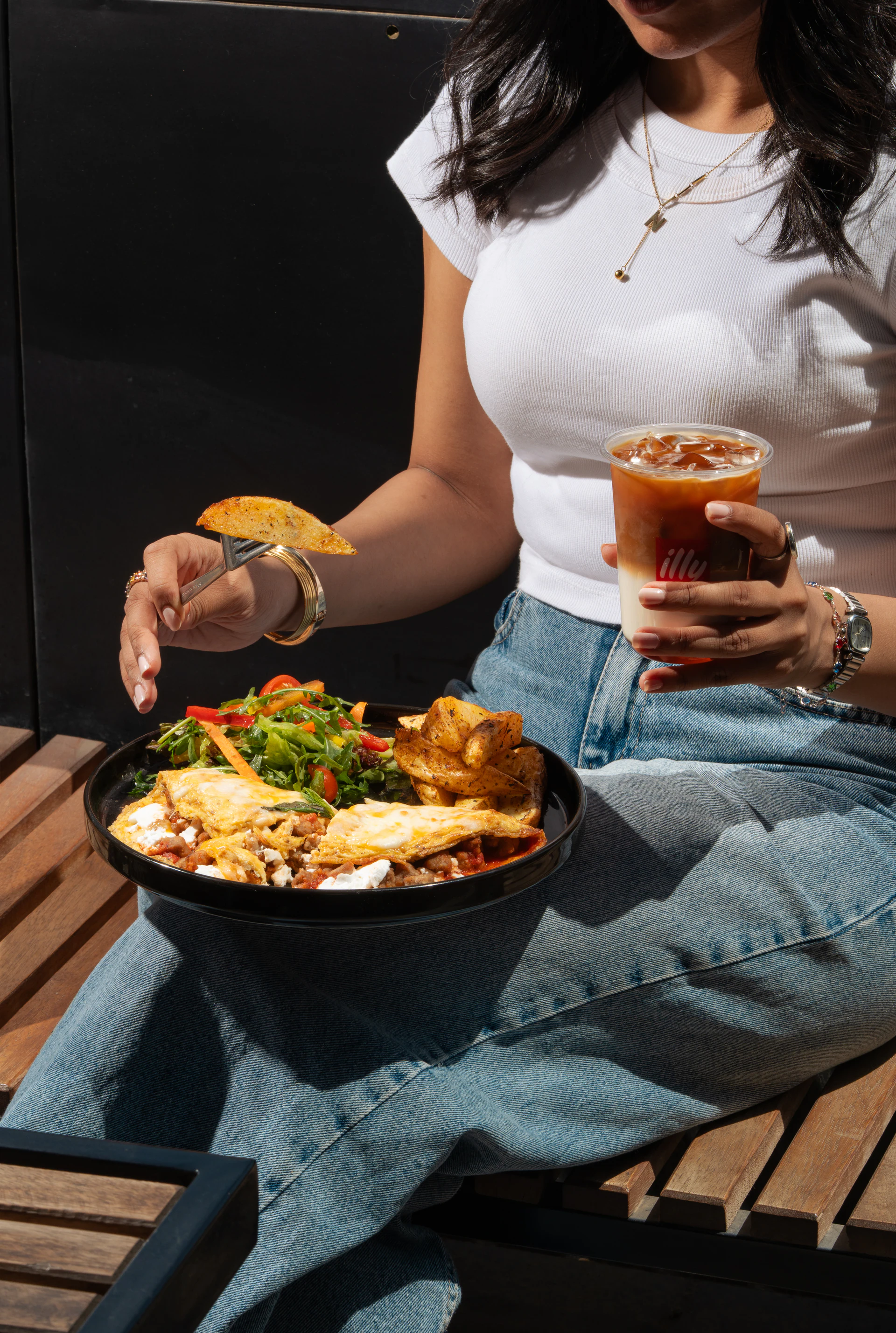 Café guest holding an iced illy coffee with a plated meal