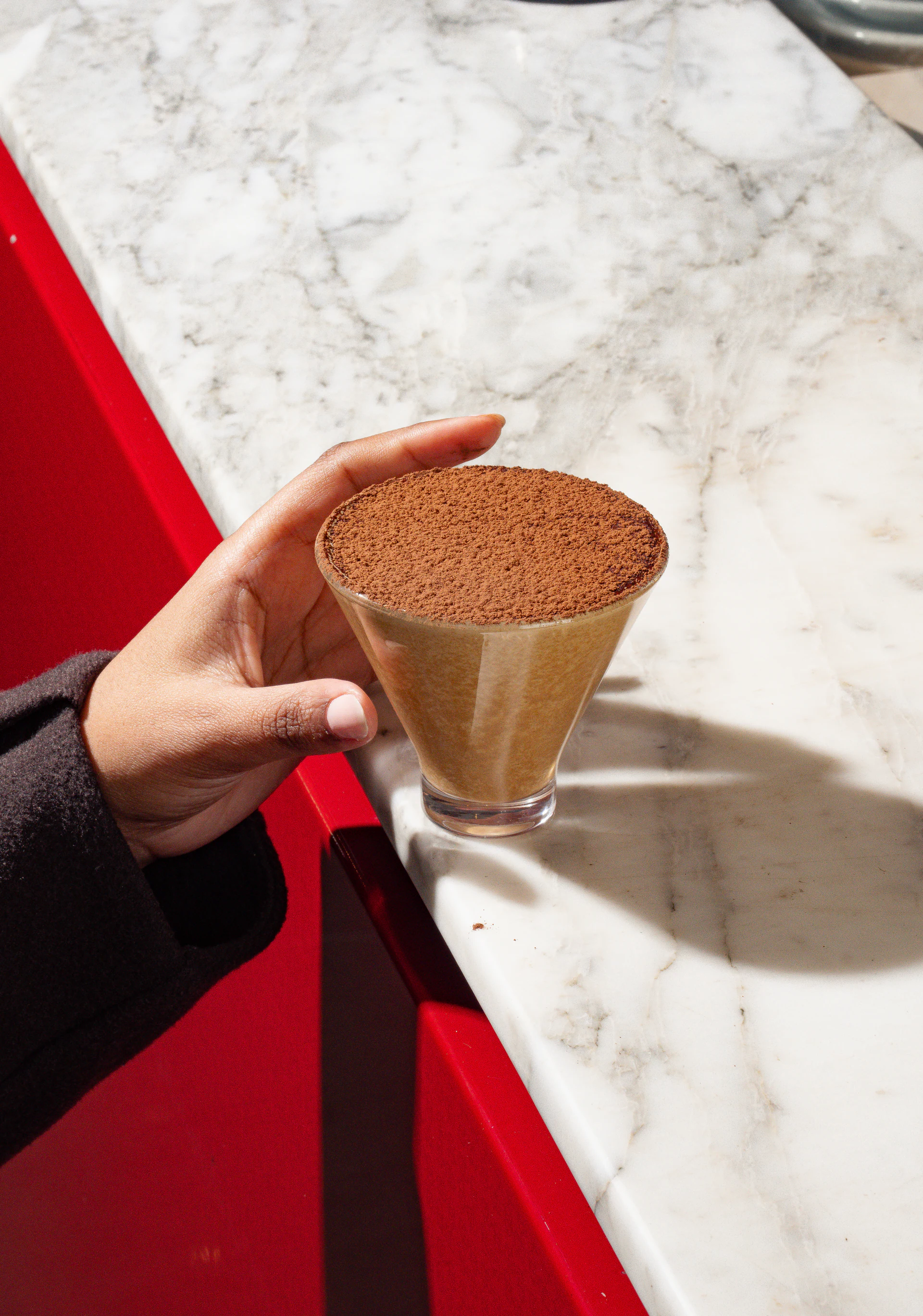 Guest holding an illymisu dessert glass beside a red café chair