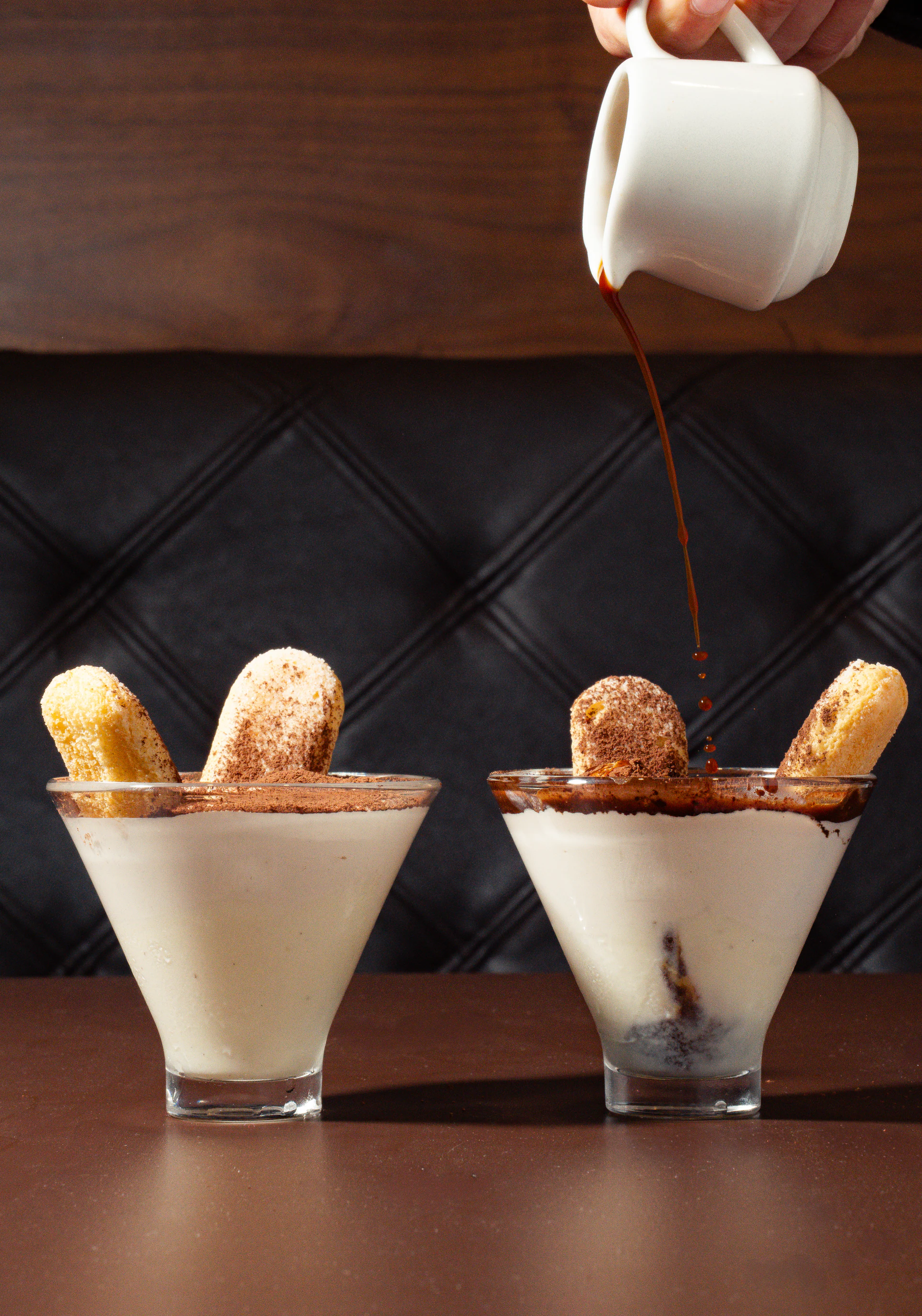 Two illymisu dessert glasses topped with ladyfingers and cocoa