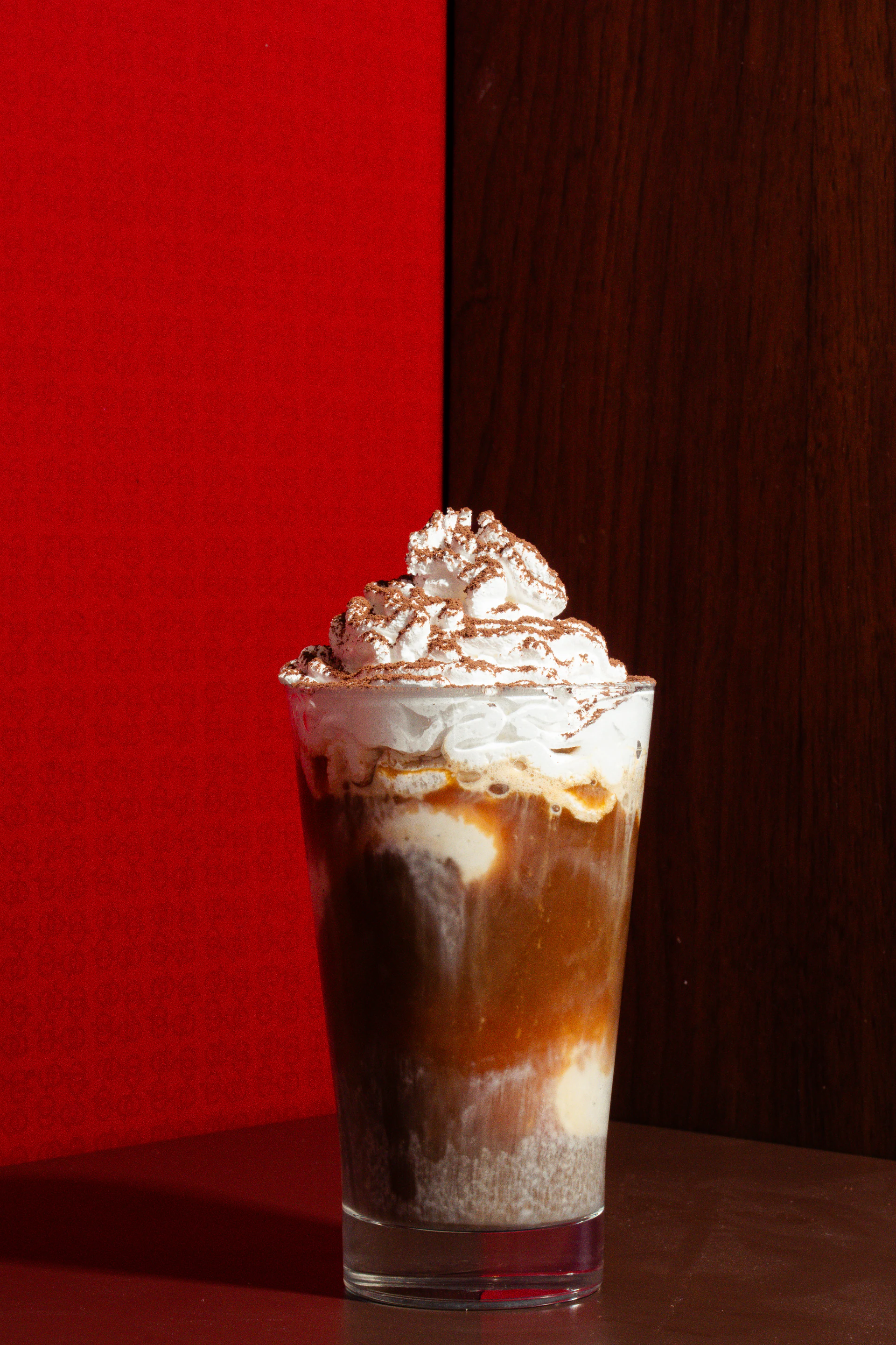 Iced illy coffee topped with whipped cream against a red backdrop