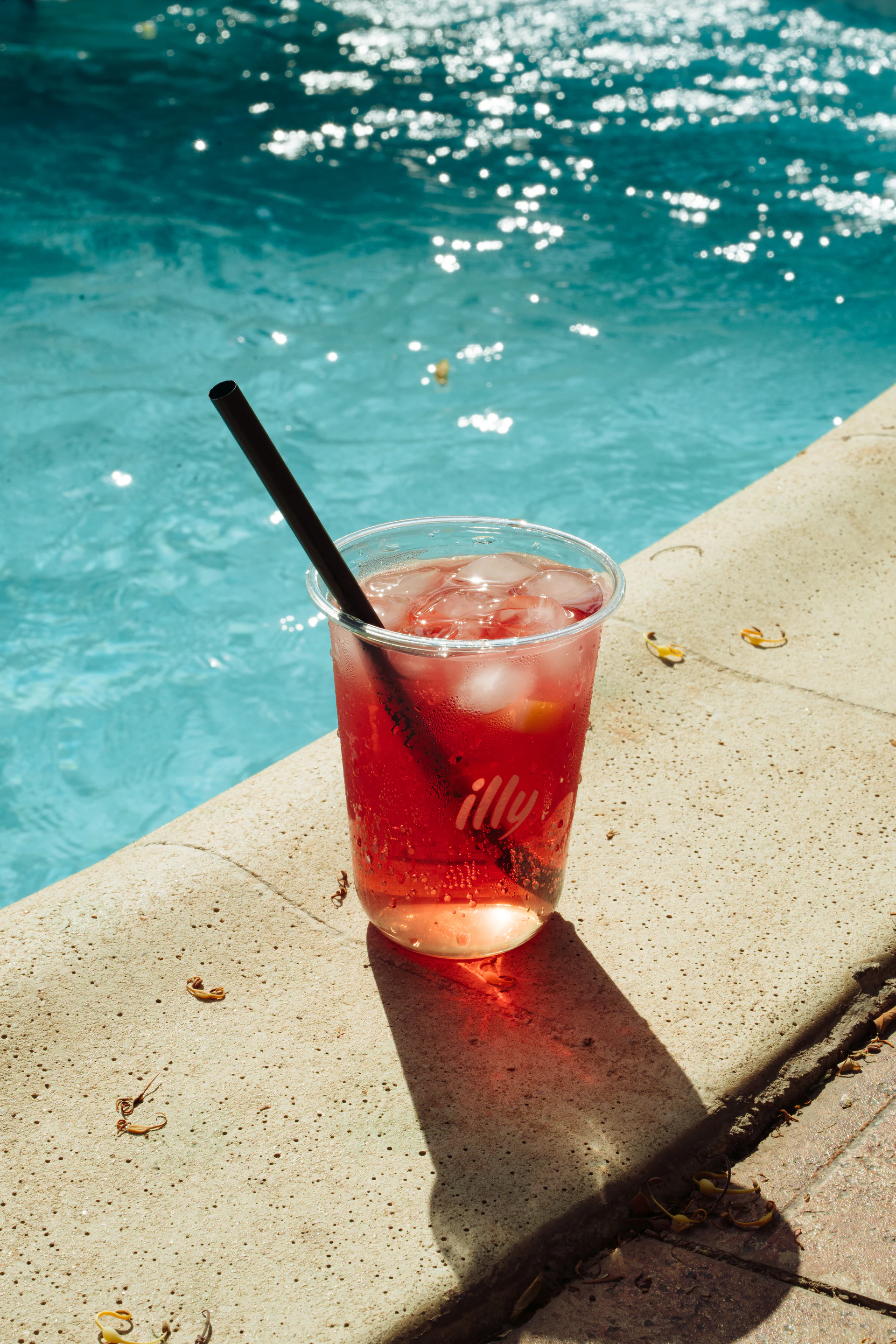 Red iced illy drink beside a sunlit swimming pool