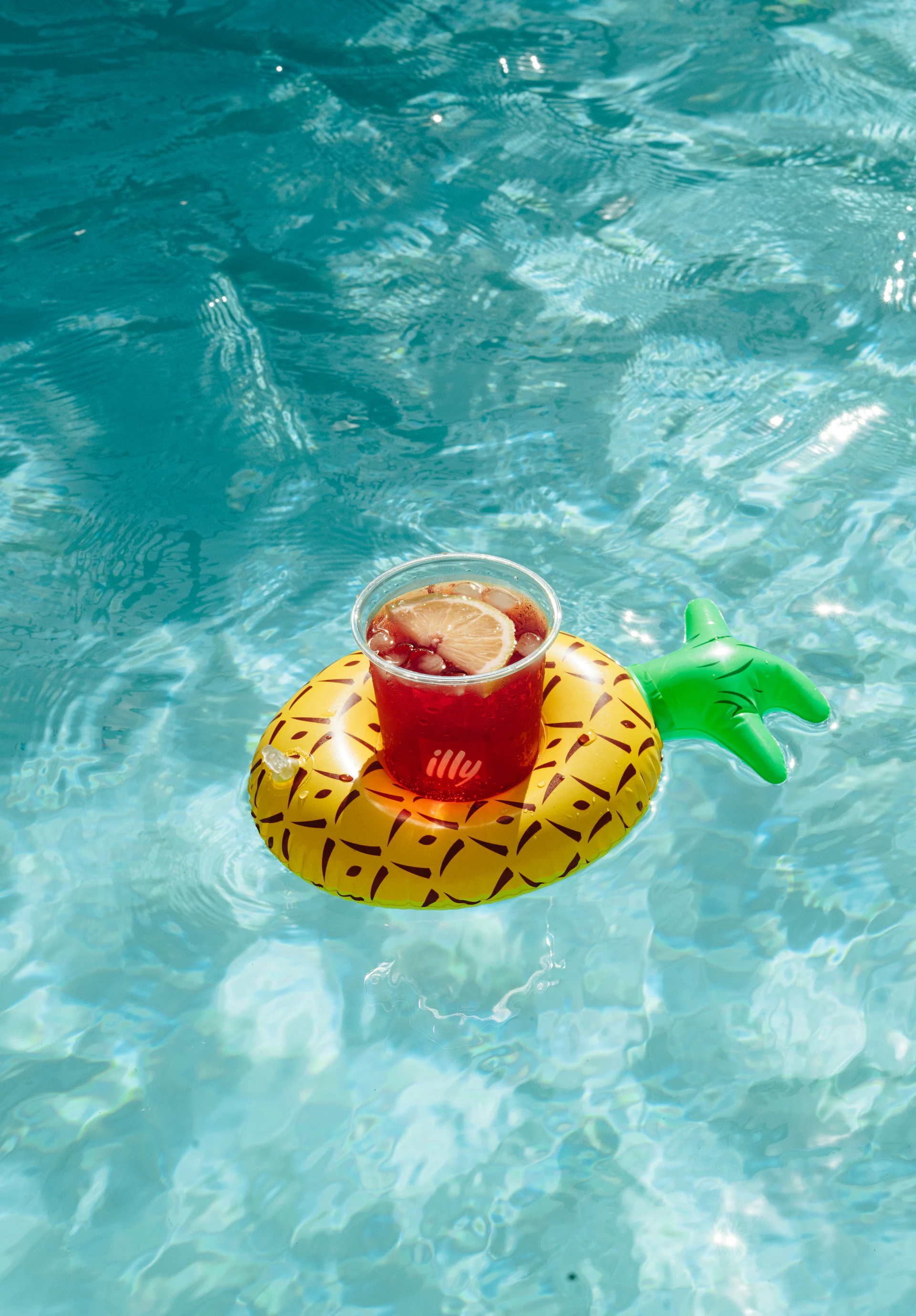 Red illy drink floating in a pineapple holder in the pool