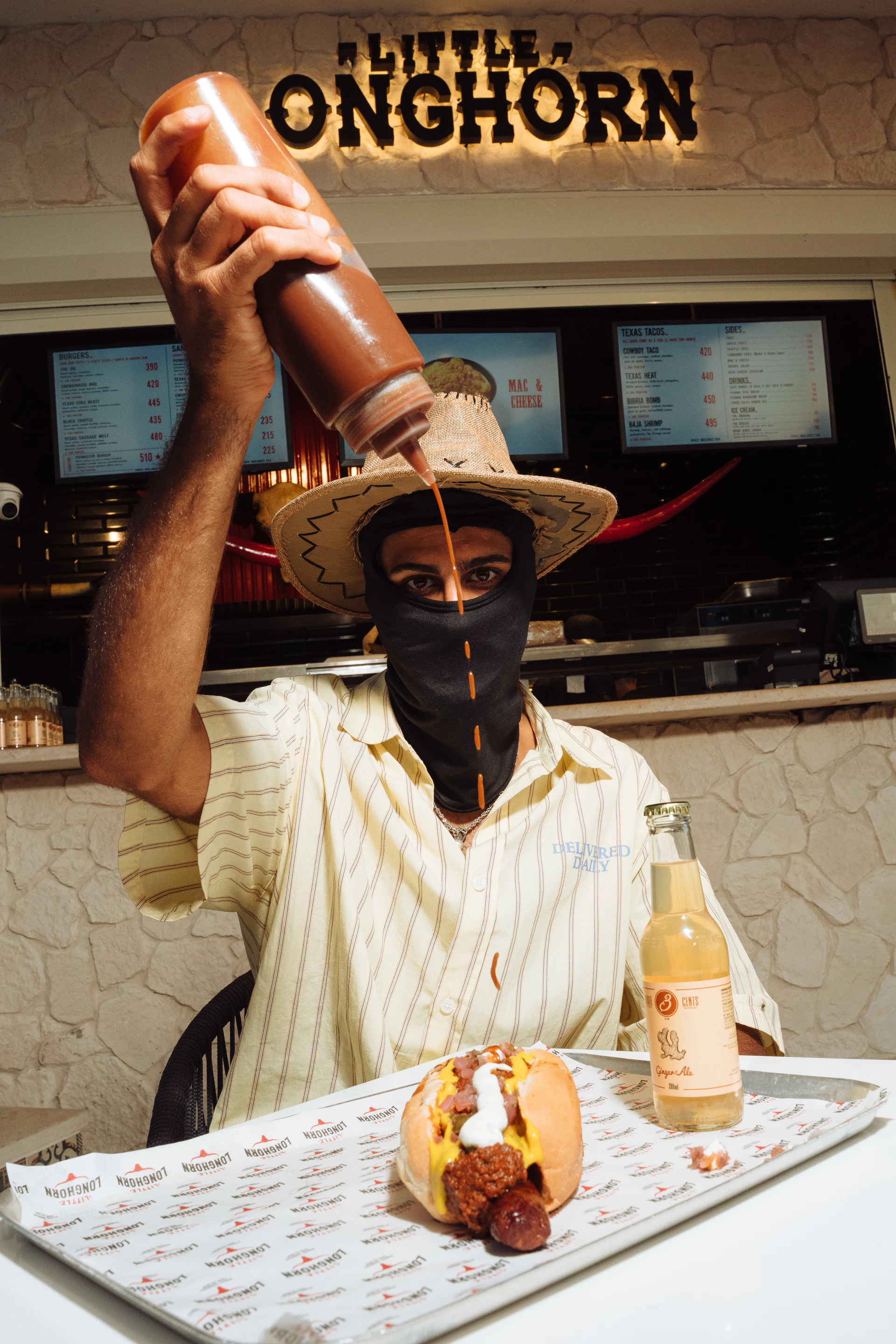 Masked Little LongHorn outlaw pouring sauce over a hot dog